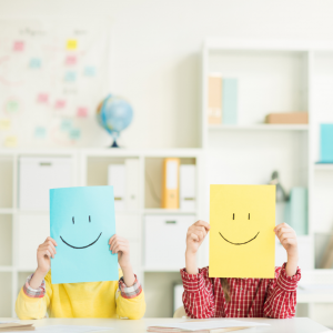 Two people holding smiley face papers in front of their faces.