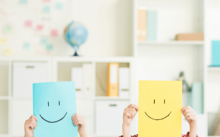 Two people holding smiley face papers in front of their faces.